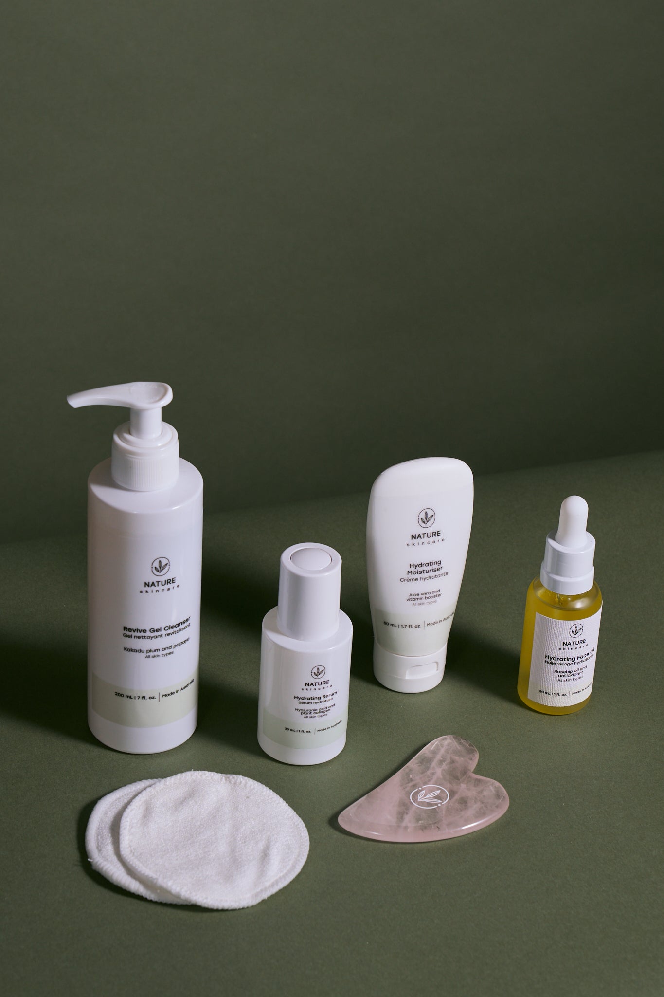Nature Skincare natural skincare routine including revive gel cleanser, hydrating serum, hydrating moisturiser, face oil, reusable organic cotton pads and rose quartz gua sha on green background