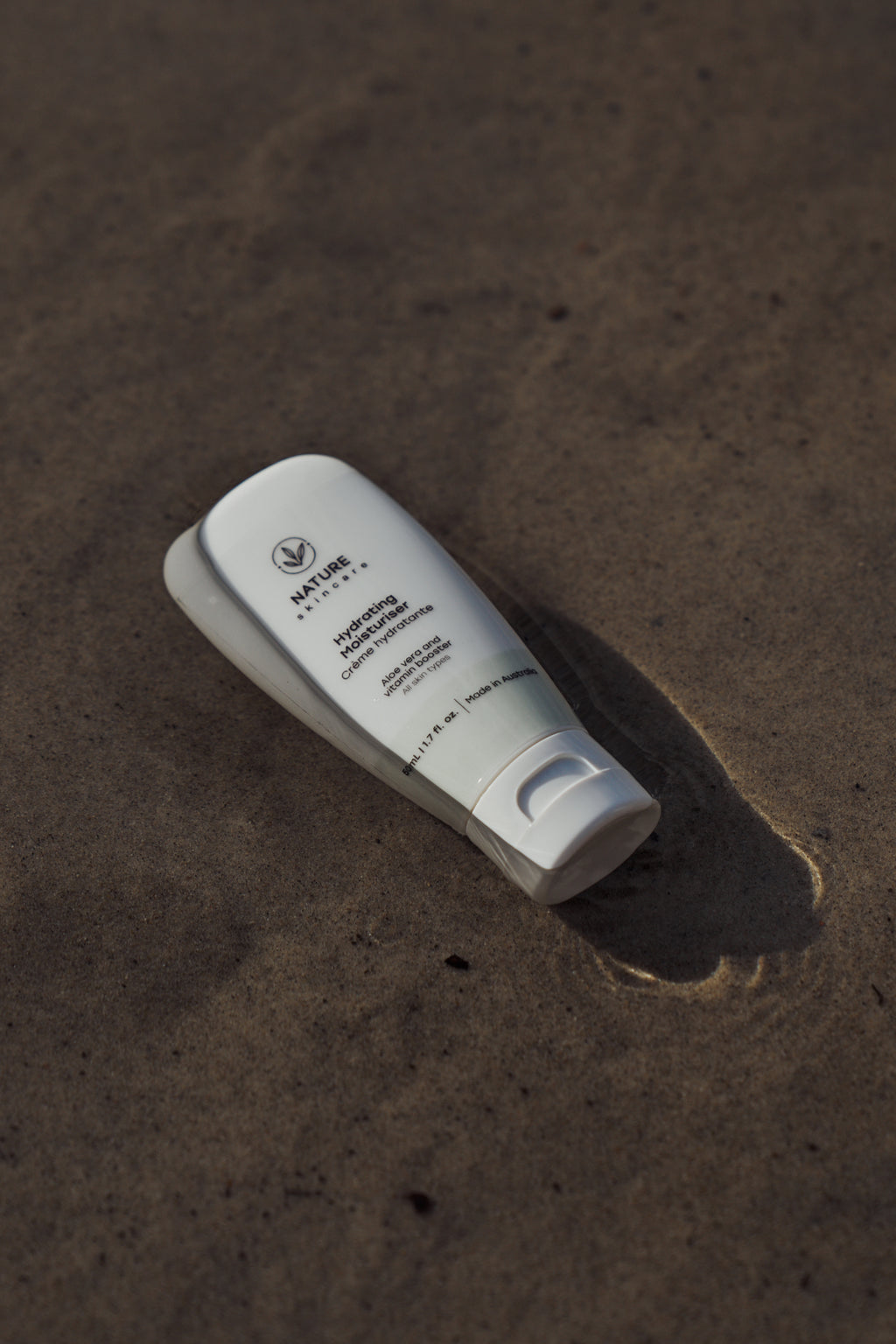 Australian organic hydrating moisturiser tube lying on sand in natural light