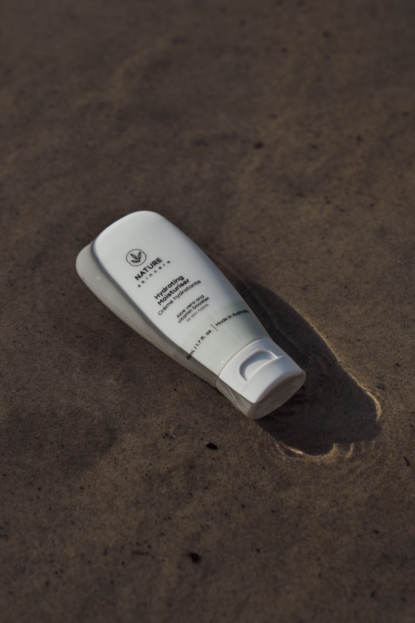 Australian organic hydrating moisturiser tube lying on sand in natural light