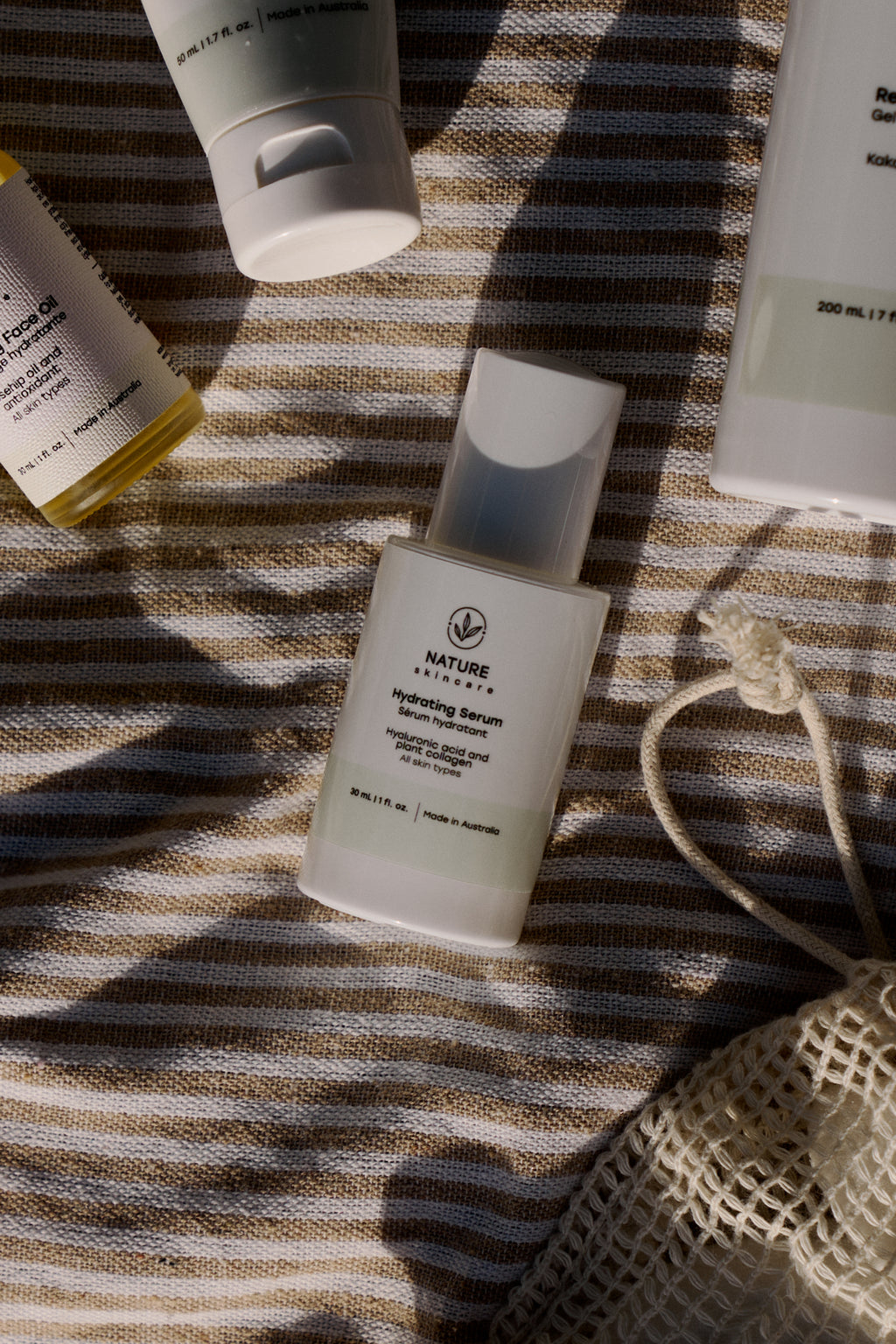 Hydrating serum bottle lying on striped fabric with other skincare products around it