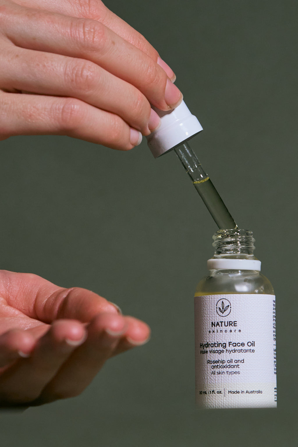 Hand holding a dropper over a bottle of Nature Skin care Hydrating Face Oil with a neutral background.
