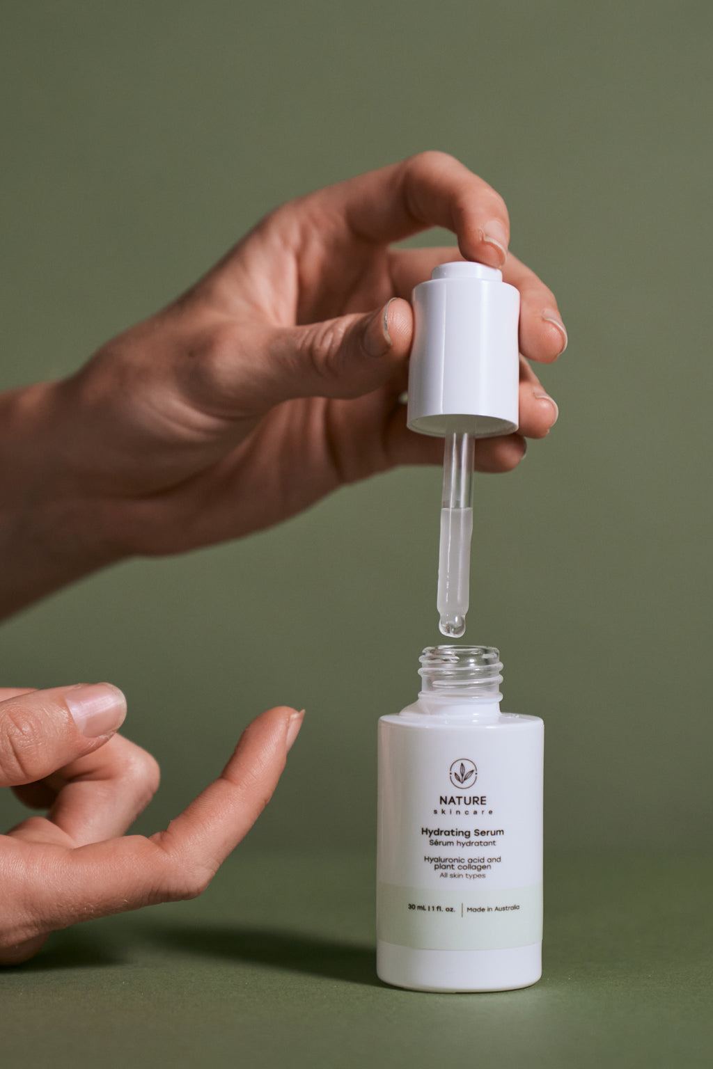 Hand holding a dropper over a white skincare serum bottle with a green background