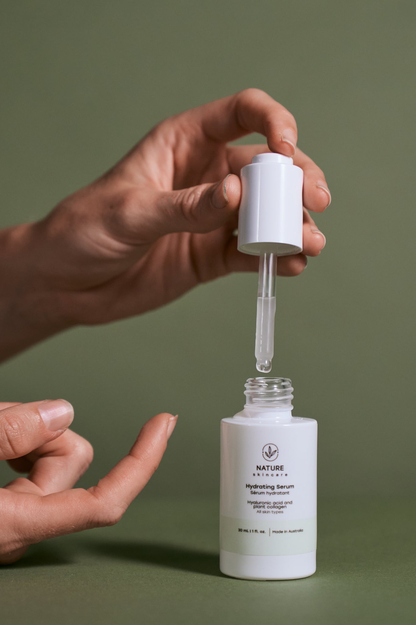 Hand holding a dropper over a white skincare serum bottle with a green background