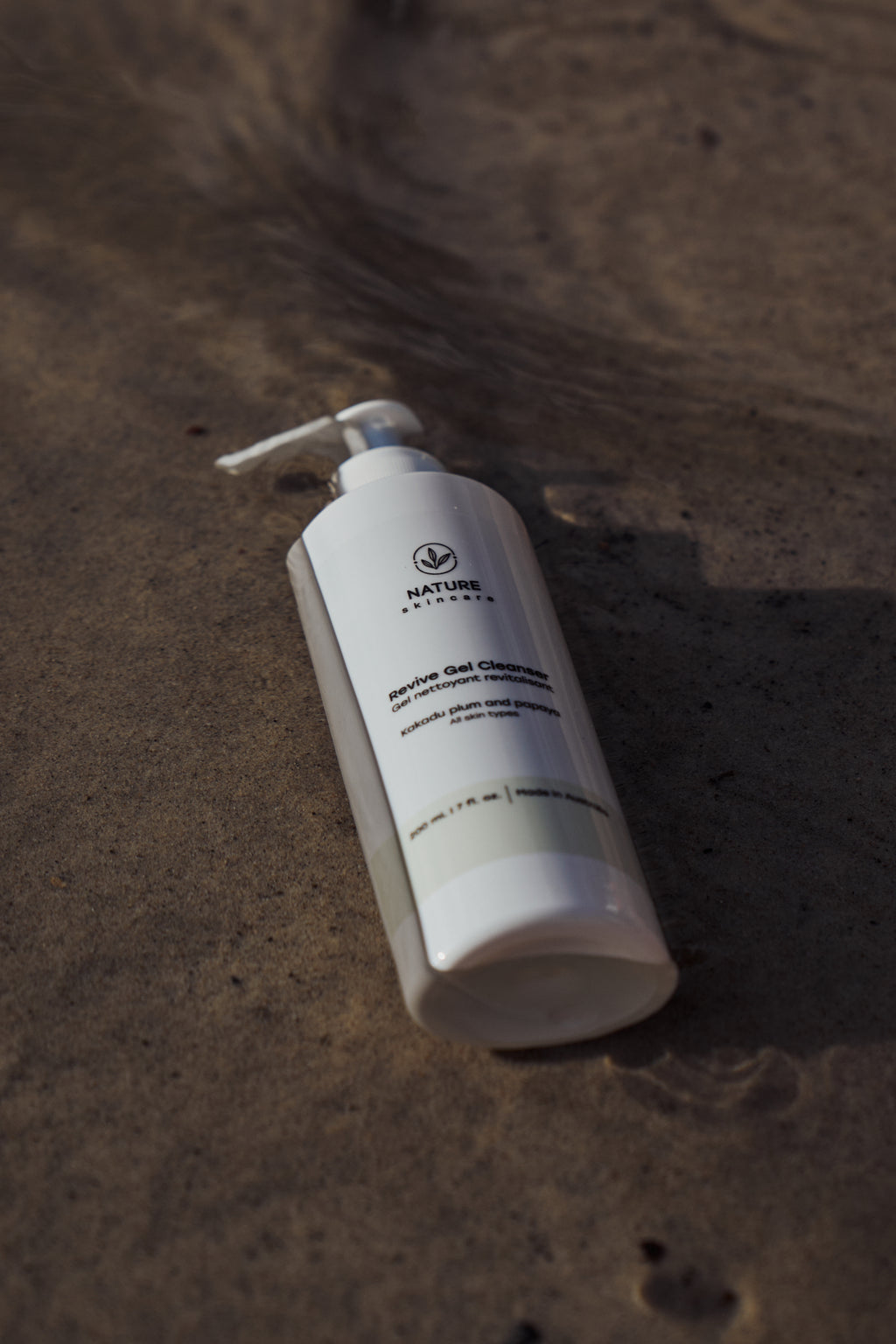 Organic revive gel cleanser bottle lying on sand in natural light